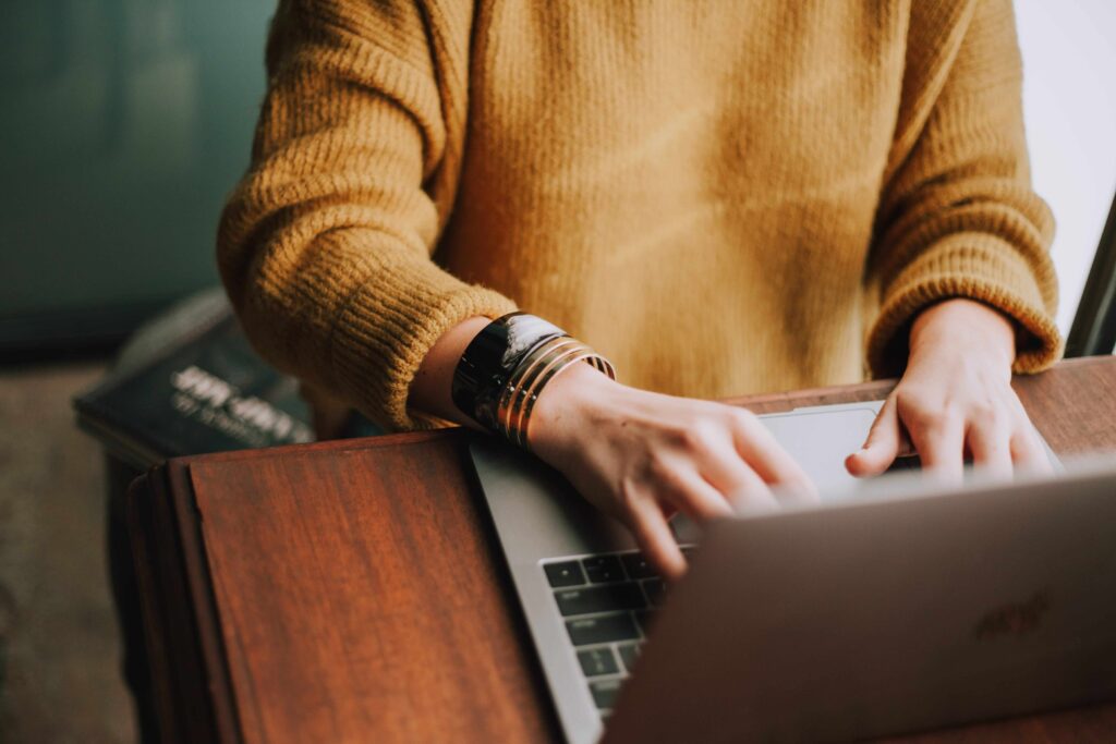 A woman hands wearing yellow sweater typing on her laptop